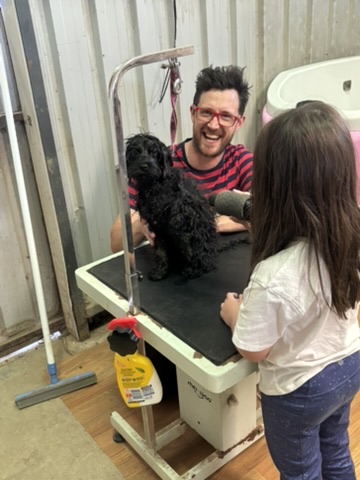 Bradley smiling while helping a young person learn dog grooming